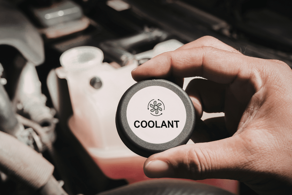 Antifreeze vs. Coolant in Tea, SD by Sioux Empire Automotive Service Center. Image of a technician holding a coolant reservoir cap labeled “Coolant” above the engine bay, highlighting coolant level checks to help prevent overheating and protect engine performance.