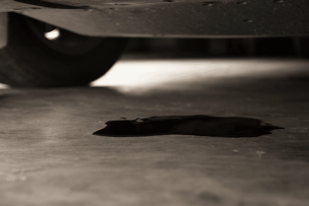 Jeep and Chrysler 3.6L Oil Leak Repair in Tea, SD, at Sioux Empire Automotive Service Center. Image of oil leaking from the underside of a vehicle onto the shop floor, indicating a fluid leak requiring professional diagnosis and repair.