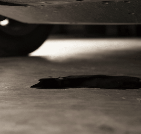 Jeep and Chrysler 3.6L Oil Leak Repair in Tea, SD, at Sioux Empire Automotive Service Center. Image of oil leaking from the underside of a vehicle onto the shop floor, indicating a fluid leak requiring professional diagnosis and repair.