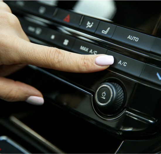 10 signs your car needs a/c repair, auto repair in Tea, SD at Sioux Empire Automotive Service Center. Close-up of a hand pressing the A/C button on a modern vehicle's climate control panel.